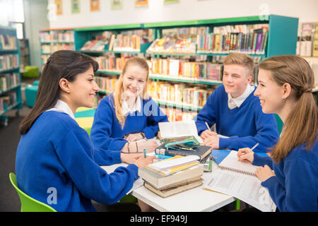 Four teenage students studying together at table in library Stock Photo