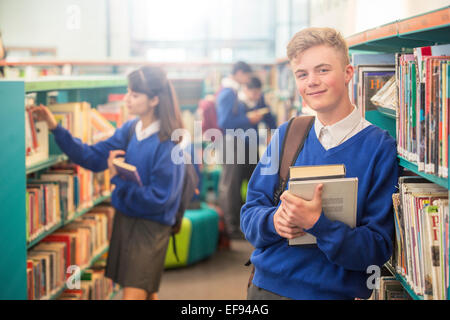Portrait of smiling male student wearing blue school uniform holding books in library Stock Photo