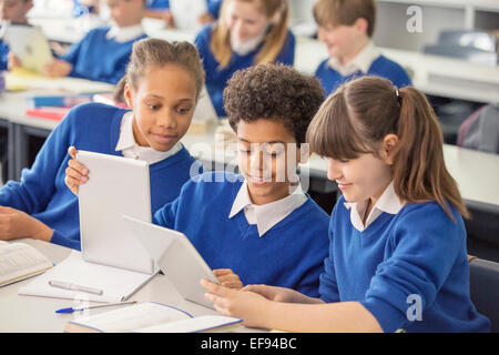 Elementary school children wearing blue school uniforms using digital tablets at desk in classroom Stock Photo