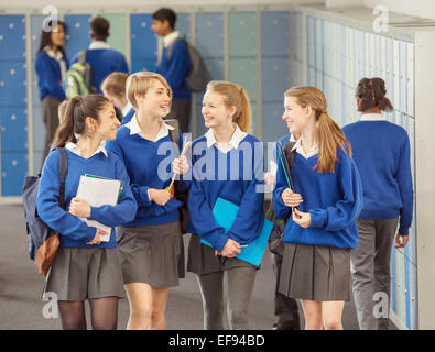 Cheerful female students wearing blue school uniforms walking in locker room Stock Photo
