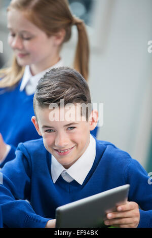 Portrait of cheerful schoolboy wearing blue school uniform with tablet pc in classroom Stock Photo