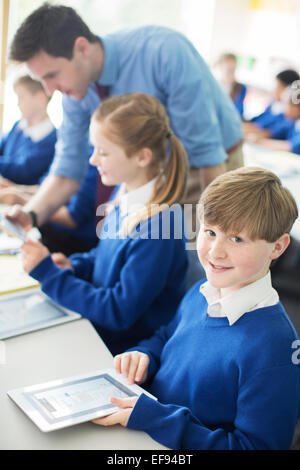 Portrait of schoolboy sitting with digital tablet in classroom, children and teacher in background Stock Photo