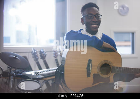 Smiling college student sitting with acoustic guitar in classroom Stock Photo
