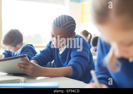 Schoolboy wearing school uniform writing at desk in classroom Stock Photo