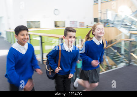 Happy pupils wearing school uniforms running in school corridor Stock Photo