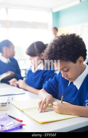 Schoolboy drawing in notebook at desk in classroom, girls in background Stock Photo