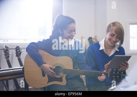 Female students playing acoustic guitar in classroom and using tablet pc Stock Photo