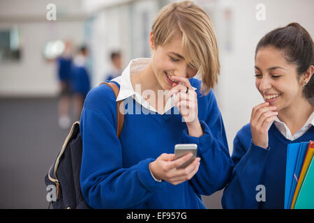 Two smiling female students looking at mobile phone in school corridor Stock Photo