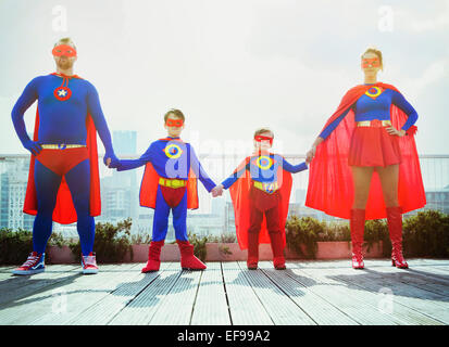 Superhero family holding hands on city rooftop Stock Photo