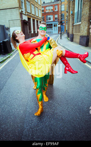 Superhero carrying wife on city street Stock Photo