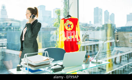 Businesswoman talking on cell phone with superhero costume behind her Stock Photo