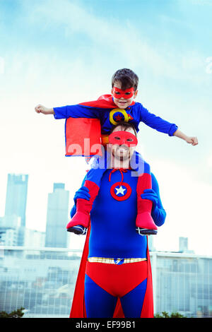 Superhero father carrying son on shoulders on city rooftop Stock Photo