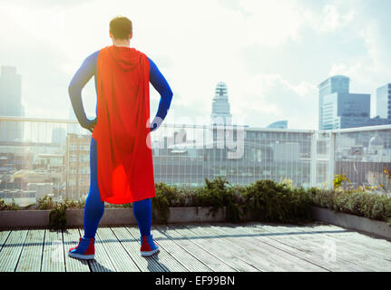 Superhero looking at view from city rooftop Stock Photo