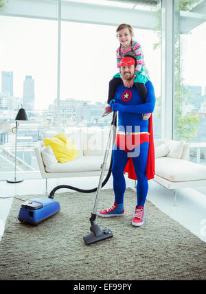 Superhero father vacuuming and carrying daughter on shoulders Stock Photo
