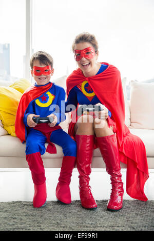 Superhero mother and son playing video game in living room Stock Photo