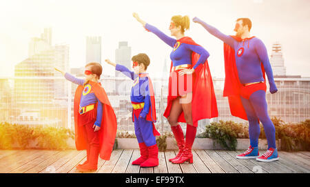 Superhero family standing with arms outstretched on city rooftop Stock Photo