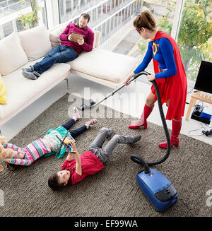 Superhero vacuuming around family in living room Stock Photo