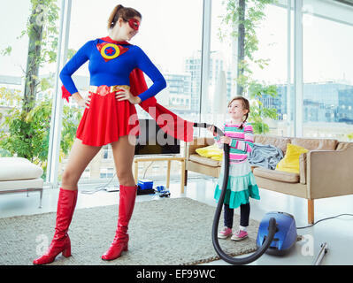 Daughter of superhero vacuuming her cape in living room Stock Photo