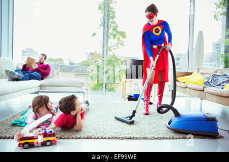 Superhero vacuuming around family in living room Stock Photo