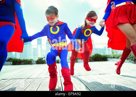 Family of superheroes running on city rooftop Stock Photo