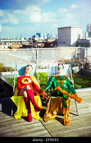 Superhero couple sitting on city rooftop Stock Photo