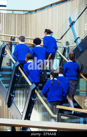 Rear view of group of pupils wearing blue school uniforms walking up stairs in school Stock Photo
