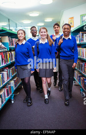 Students wearing school uniforms walking between bookshelves in library Stock Photo