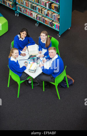 Overhead view of four students doing their homework at round table, looking at camera Stock Photo