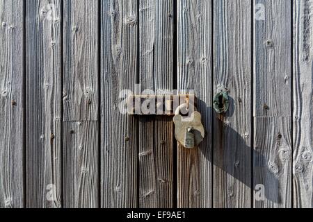 Old weathered and rusting metal latch and padlock on an old weathered wooded slatted door.  Picture includes a metal keyhole. Stock Photo