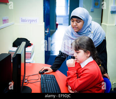 Muslim teacher in headscarf helping pupil with computer work Stock Photo