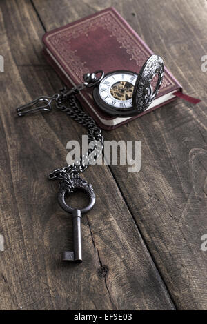 Vintage grunge still life with  pocket watch, old brass key and tattered book. Stock Photo