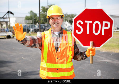 Friendly construction worker in the road holding up a stop sign. Stock Photo