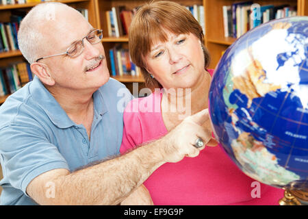 Adult students in library using a globe to study geography. Stock Photo