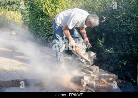 A builder uses an angle grinder to cut bricks while laying a patio. Stock Photo