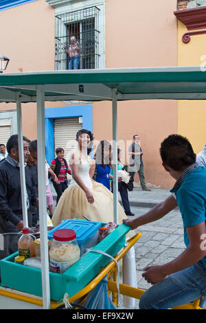 Oaxaca, Mexico - A quinceañera celebration. A street vendor watches as a girl celebrating her 15th birthday walks in the street. Stock Photo