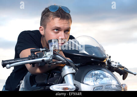 young man with a stubborn look leaned on the steering wheel of his bike Stock Photo