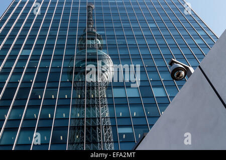 Tokyo Skytree is reflected in a tall building with a CCTV camera on a wall to the right. Oshiage, Tokyo, Japan Stock Photo