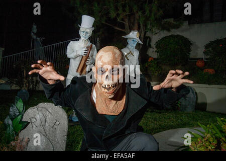 Wearing a monster fright mask a young man gets into the spirit of a Halloween night 'haunted mansion' in Lake Forest, CA. Note ghostly figures in background. Stock Photo