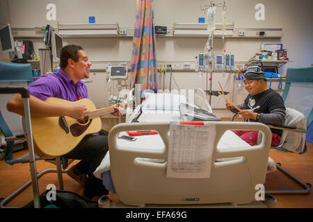 A music therapist playing a guitar entertains a young boy patient at CHOC Children's Hospital in Orange, CA. Note child playing on drums. Stock Photo