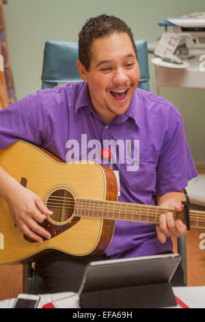 A happy Hispanic music therapist plays guitar and sings for a young patient at CHOC Children's Hospital in Orange, CA Stock Photo