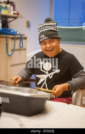 A young Hispanic patient at CHOC Children's Hospital, Orange, CA, plays electronic drums as he listens to the playing of a music therapist. Stock Photo