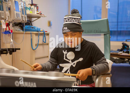 A young Hispanic patient at CHOC Children's Hospital, Orange, CA, plays electronic drums as he listens to the playing of a music therapist. Stock Photo