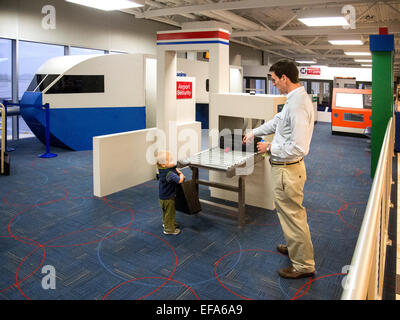 A father and his toddler son play in the 1,500-square-foot  Lambert-St.Louis Airport 'Play Port' where children waiting for a flight can work off some of their energy. It includes a child-sized plane, an air traffic control tower with a slide, car rental counters, a luggage conveyor belt and an airport screening area with a pretend x-ray machine. Stock Photo