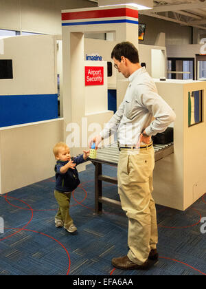 A father and his toddler son play in the 1,500-square-foot  Lambert-St.Louis Airport 'Play Port' where children waiting for a flight can work off some of their energy. It includes a child-sized plane, an air traffic control tower with a slide, car rental counters, a luggage conveyor belt and an airport screening area with a pretend x-ray machine. Stock Photo