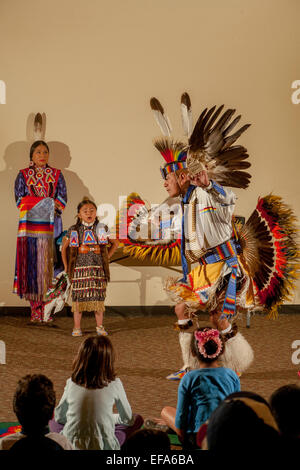 As children in the audience watch, a  Navajo Indian dancer wearing full tribal costume performs the Fancy Thunder Dance during an evening of Native American culture at the Laguna Niguel, CA, public library. Note costumed daughters. Stock Photo
