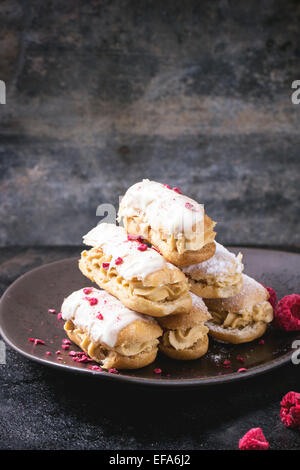Ceramic plate of mini eclairs with white chocolate, served with dry raspberry on dark background Stock Photo