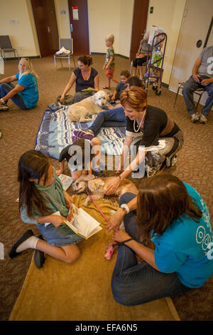 Children read to licensed therapy dogs in at 'Tales For Tails,' confidence building activity at a public library in Laguna Niguel, CA.  Note librarian petting dog and owners in T shirts. Stock Photo