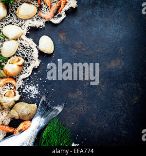 Delicious fresh fish and seafood on dark vintage background. Fish, clams and  shrimps with aromatic herbs, spices and vegetables Stock Photo