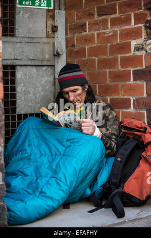 A homeless man reading a book while in his sleeping bag Stock Photo