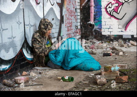 A homeless man reading a book while in his sleeping bag Stock Photo